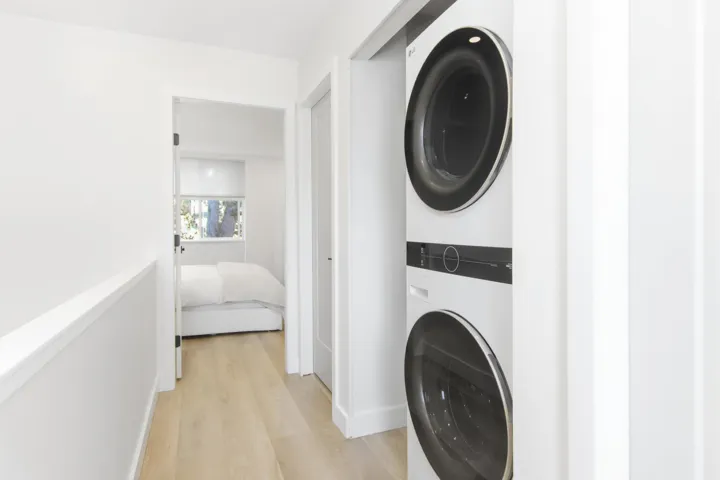 Stacked laundry unit featuring a white finish with metallic trim, wood-finish flooring, and crisp white wall paint