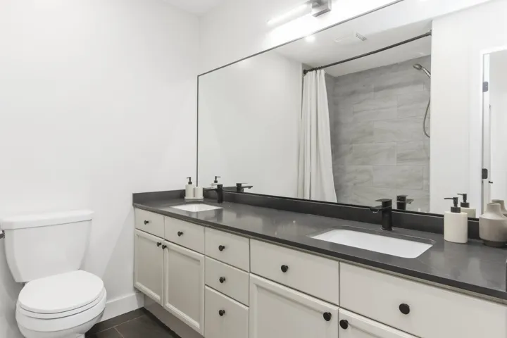Bathroom featuring a double-sink vanity with a solid-surface countertop, rectangular undermount sinks, matte black fixtures, and a full-width mirror