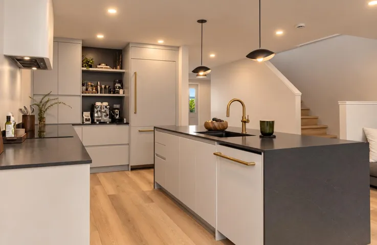 Kitchen featuring matte flat-panel cabinetry, dark stone-finish countertops, an integrated refrigerator, recessed lighting, and a central island with a gold-tone gooseneck faucet