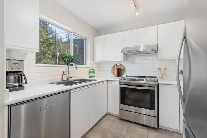 Kitchen with under cabinet range hood, appliances with stainless steel finishes, white cabinetry, and a sink