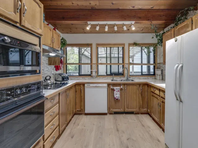 Kitchen with white appliances, under cabinet range hood, light wood-style floors, backsplash, skylight and exposed beams