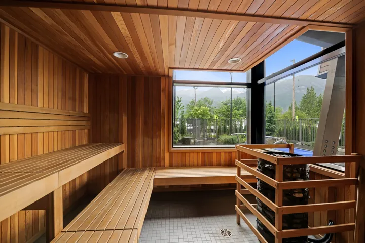 Cedar-lined sauna featuring multi-level slatted benches, a built-in heater, recessed ceiling lighting, and large exterior windows showcasing mountain scenery