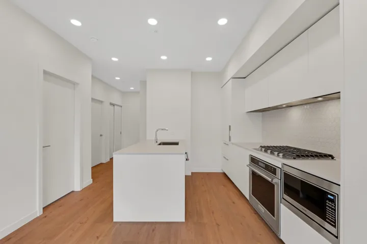 Modern kitchen featuring a central island with an undermount sink, white flat-panel cabinetry, stainless steel appliances, a gas cooktop, and hexagonal tile backsplash