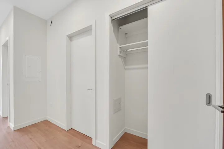 Hallway featuring wood-finish flooring, white walls, and a built-in closet with shelving and hanging rod