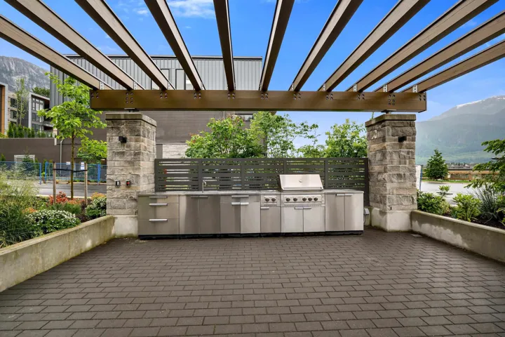 Outdoor kitchen featuring a built-in grill, stainless steel cabinetry, and an integrated sink, all under a decorative pergola
