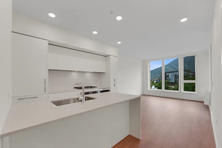 Modern kitchen featuring white flat-panel cabinetry, a light-toned countertop island with an undermount sink, and recessed lighting