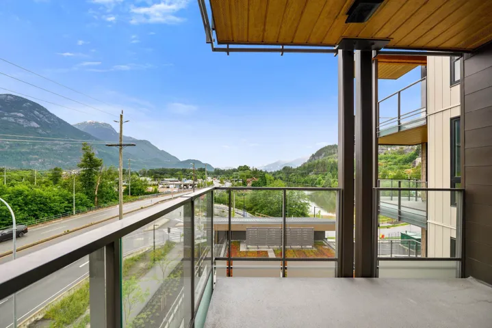 Private balcony featuring glass railings, wood-finish ceiling, concrete flooring, and views of surrounding mountains and a body of water