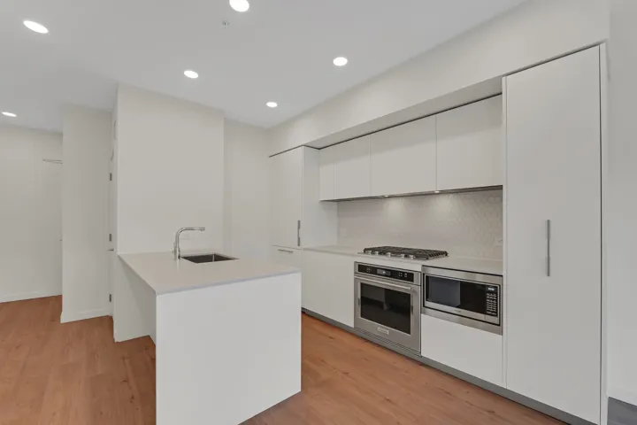 Modern kitchen featuring a central island with an undermount sink, sleek white flat-panel cabinetry, stainless steel appliances, a gas cooktop, and a hexagonal tile backsplash