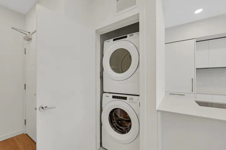 Integrated stacked washer and dryer in a dedicated closet, featuring a white solid-core door with brushed nickel hardware