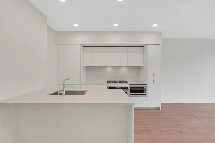 Modern kitchen featuring flat-panel cabinetry, a stainless steel sink with a gooseneck faucet, integrated cooktop, a built-in microwave, and recessed lighting
