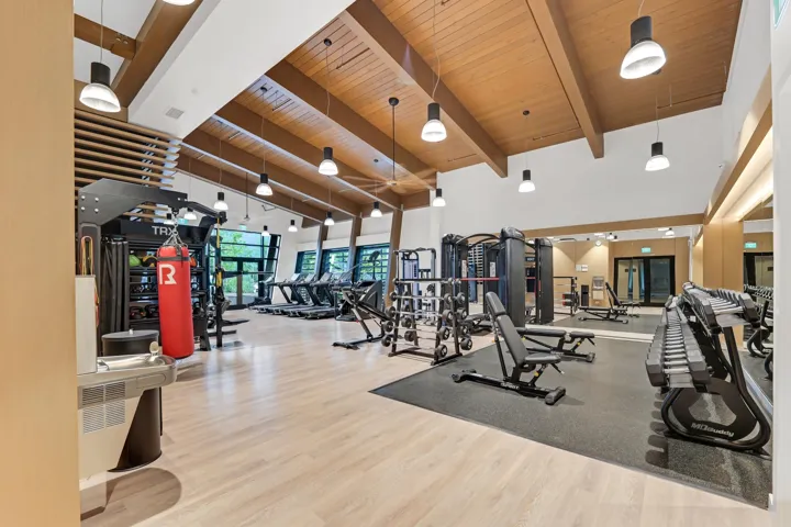 Spacious fitness center featuring wood-finish flooring, exposed wood beam ceiling, large windows, and a mirrored wall