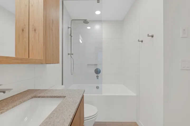 Bathroom featuring a glass-enclosed tub/shower combination with a rain shower head, white tiled walls, and recessed lighting
