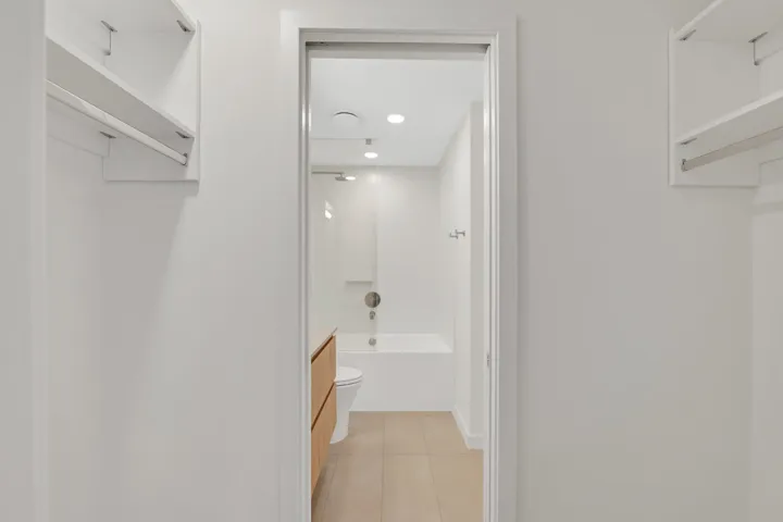 Walk-in closet featuring built-in shelving, hanging rods, and an en-suite bathroom with a soaking tub, glass shower enclosure, and wood-finish vanity