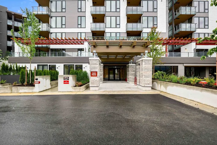 Modern multi-story building entrance featuring a prominent covered entryway, stone facade pillars, and glass doors