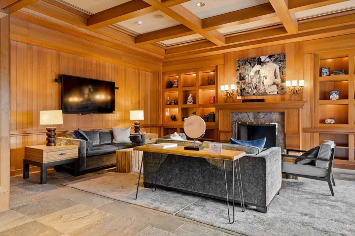Living room with built in shelves, wood walls, coffered ceiling, a high end fireplace, and stone finish floors