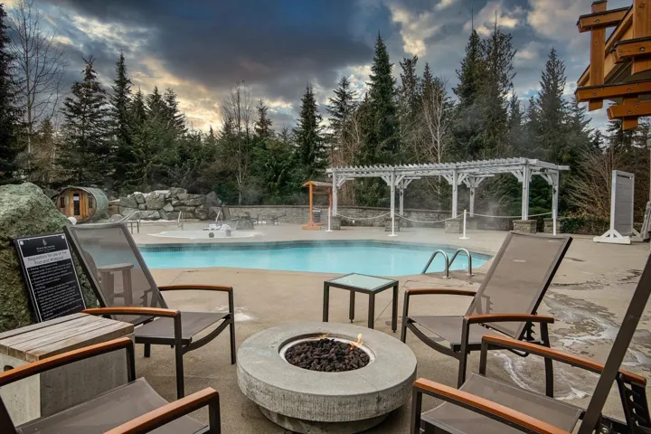 Community pool featuring a patio, a pergola, an outdoor fire pit, and view of scattered trees
