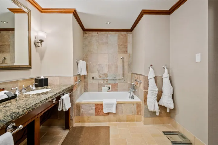 Full bathroom with tiled tub, vanity, ornamental molding, recessed lighting, and tile walls