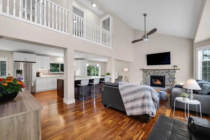 Vaulted ceiling living room featuring a stone-clad fireplace and wood-finish flooring