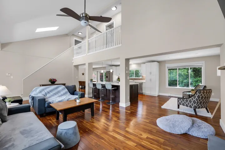 Open-concept living area featuring rich wood-finish flooring, a vaulted ceiling with a ceiling fan, and a loft overlook