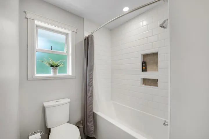 Bathtub with subway tile surround featuring two recessed niches, showerhead, and curved shower rod