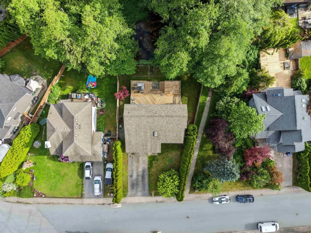Gabled roofline residence featuring a driveway with parking, front lawn, and mature perimeter hedging