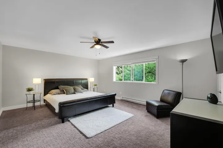 Spacious room featuring neutral painted walls, textured carpeting, a multi-pane window with white trim, and a ceiling fan with integrated lighting
