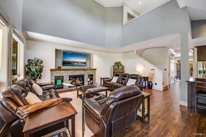 Living room with a towering ceiling, dark wood-style floors, a stone fireplace, and baseboards