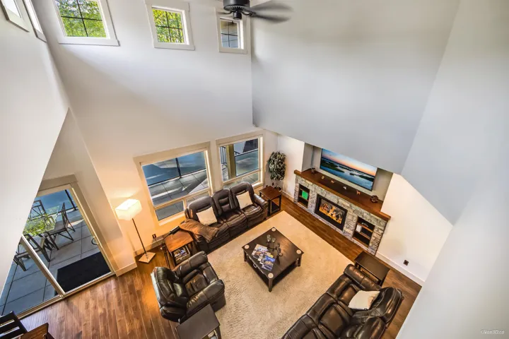 Living room featuring a towering ceiling, wood finished floors, ceiling fan, and a stone fireplace