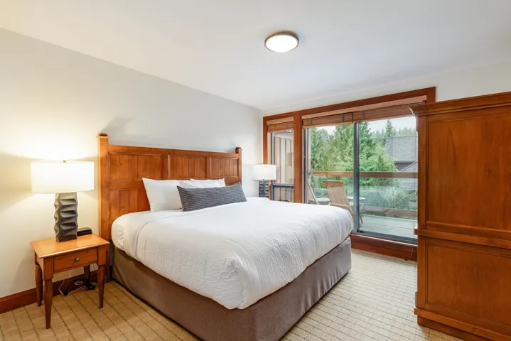 Carpeted bedroom featuring a wooden headboard and frame, a built-in wardrobe, and a sliding glass door leading to an outdoor balcony
