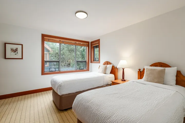 Inviting room featuring two wood-frame beds, a large window with wood trim, and neutral wall tones