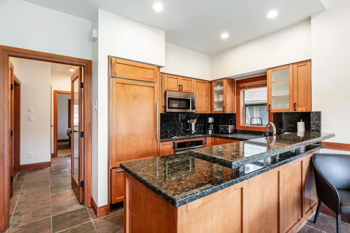 Kitchen with wood cabinetry, dark stone countertops, stainless steel appliances, and integrated refrigerator