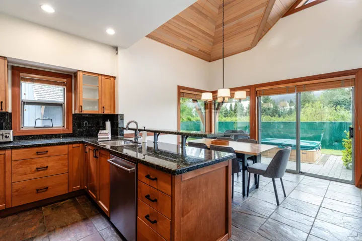Kitchen and dining area featuring warm-toned cabinetry, dark granite countertops, and a stainless steel dishwasher