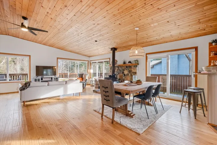 Dining room featuring a wood stove, a vaulted wooden ceiling, healthy amount of natural light, a ceiling fan, and light wood-style floors