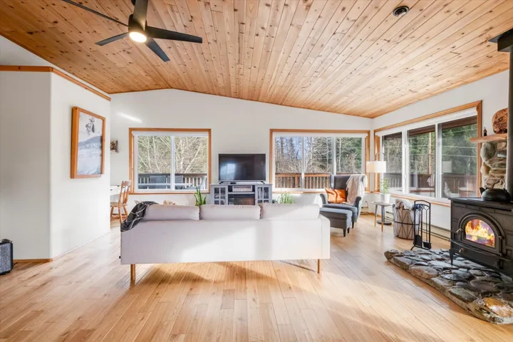 Living room with a ceiling fan, a vaulted wooden ceiling, a wood stove, and light wood-type flooring