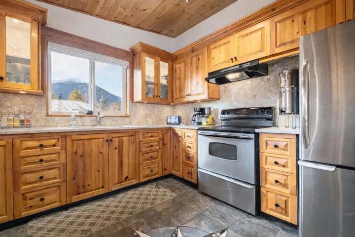 Kitchen featuring stainless steel appliances, decorative backsplash, light stone countertops, a mountain view, and wooden ceiling