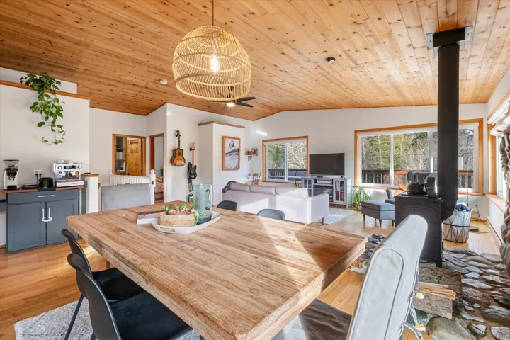 Dining space with light wood-style flooring, a vaulted wooden ceiling, and a wood stove