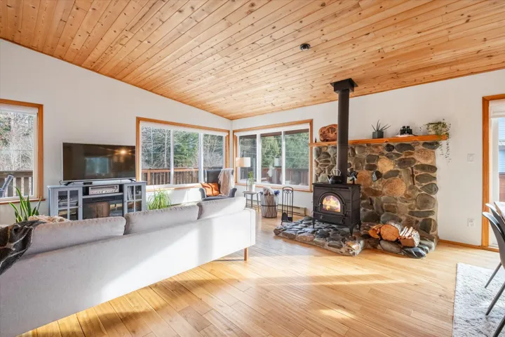 Living area with a vaulted wooden ceiling, a wood stove, and light wood-style floors