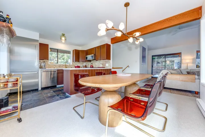 Dining area with a chandelier, beam ceiling, baseboard heating, and dark stone finish floors