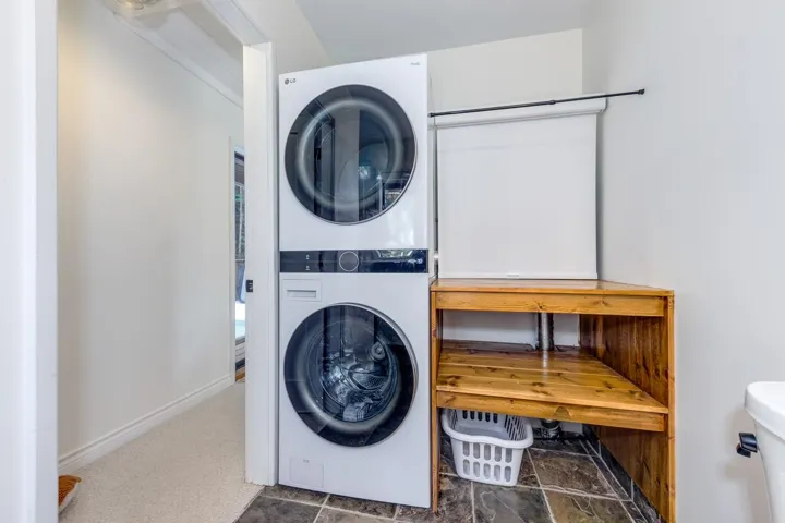 Laundry area with stacked washing machine and dryer and stone finish flooring
