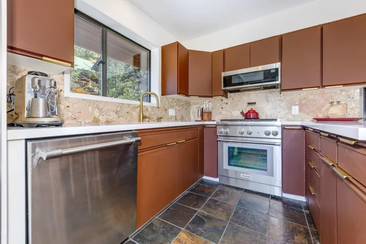 Kitchen featuring stainless steel appliances, dark stone finish floors, tasteful backsplash, and wood finish cabinets