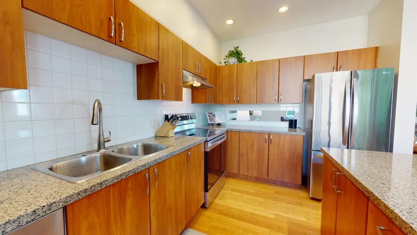 Kitchen featuring tasteful backsplash, brown cabinets, stainless steel appliances, light wood-type flooring, and under cabinet range hood
