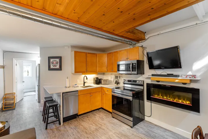 Kitchen featuring light countertops, stainless steel appliances, a glass covered fireplace, wood finish cabinetry, and wood ceiling