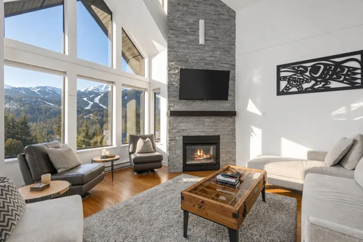 Vaulted ceilings with expansive floor-to-ceiling windows, a stone-clad fireplace, and wood-finish flooring