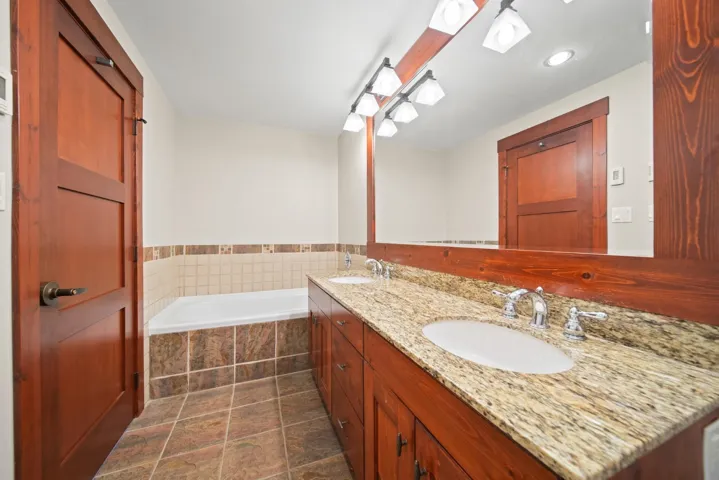 Bathroom with double vanity, a bath, recessed lighting, and dark tile patterned floors