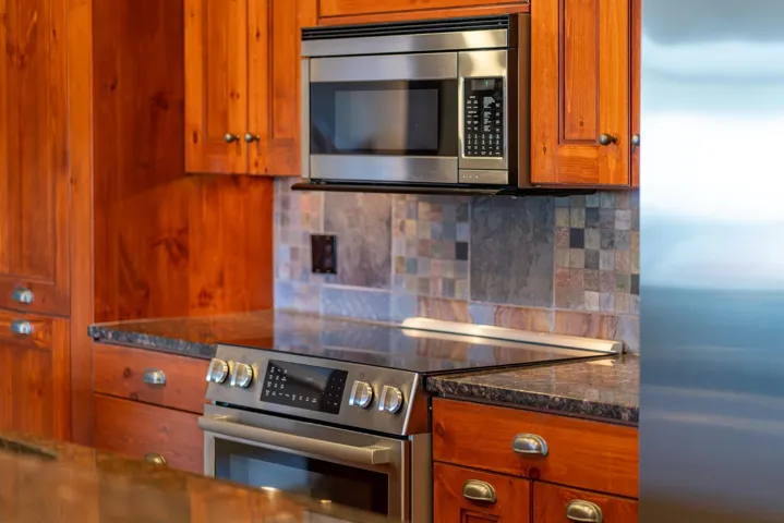 Kitchen featuring stainless steel appliances, brown cabinetry, dark stone counters, and decorative backsplash