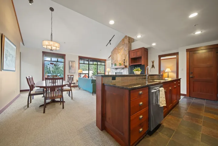 Kitchen with lofted ceiling, dark stone countertops, dishwasher, reddish brown cabinets, and open floor plan