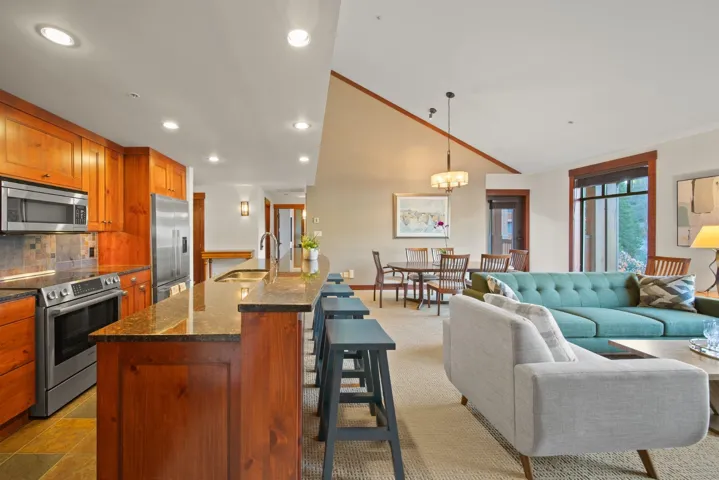 Kitchen with brown cabinets, a kitchen breakfast bar, dark stone countertops, stainless steel appliances, and decorative backsplash