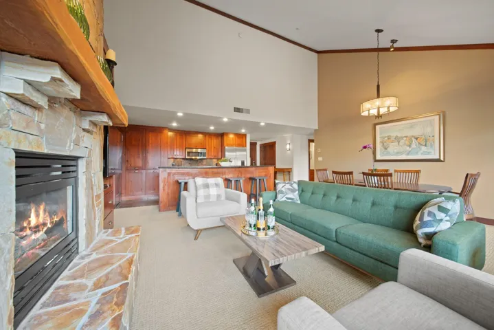 Living area featuring high vaulted ceiling, crown molding, light colored carpet, and a stone fireplace
