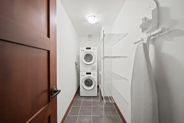 Laundry area with dark tile patterned floors and estacked washer and dryer