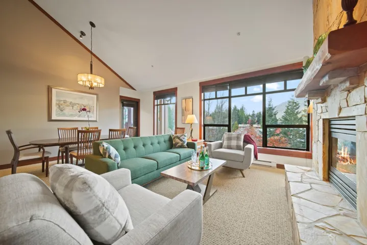 Living room with a stone fireplace, high vaulted ceiling, a chandelier, and a baseboard heating unit